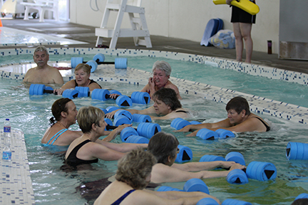 An aqua fitness class using foam barbells to reach forward and stretch.