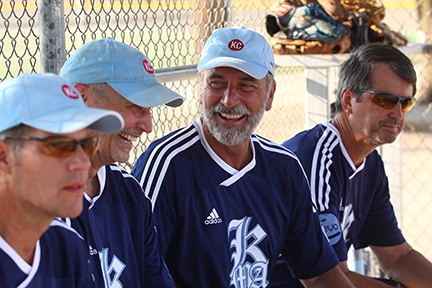 An adult softball team smiling and laughing in the dugout.