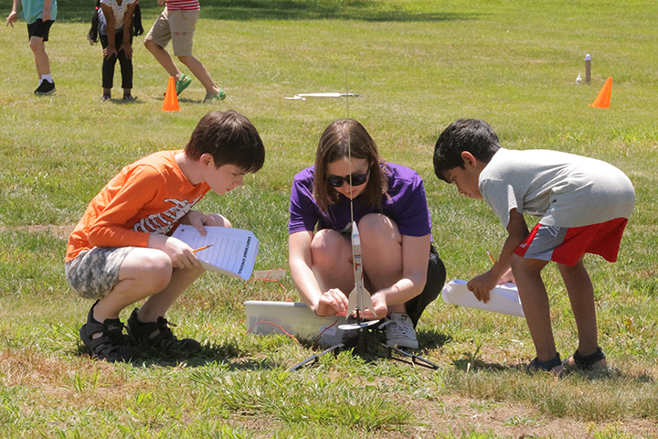 A camp instructor helps two boys shoot off a model rocket.