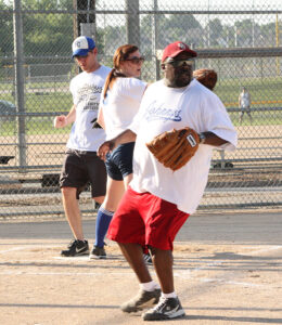 An adult softball player close to home plate awaits a ball to be thrown during an adult softball league game.