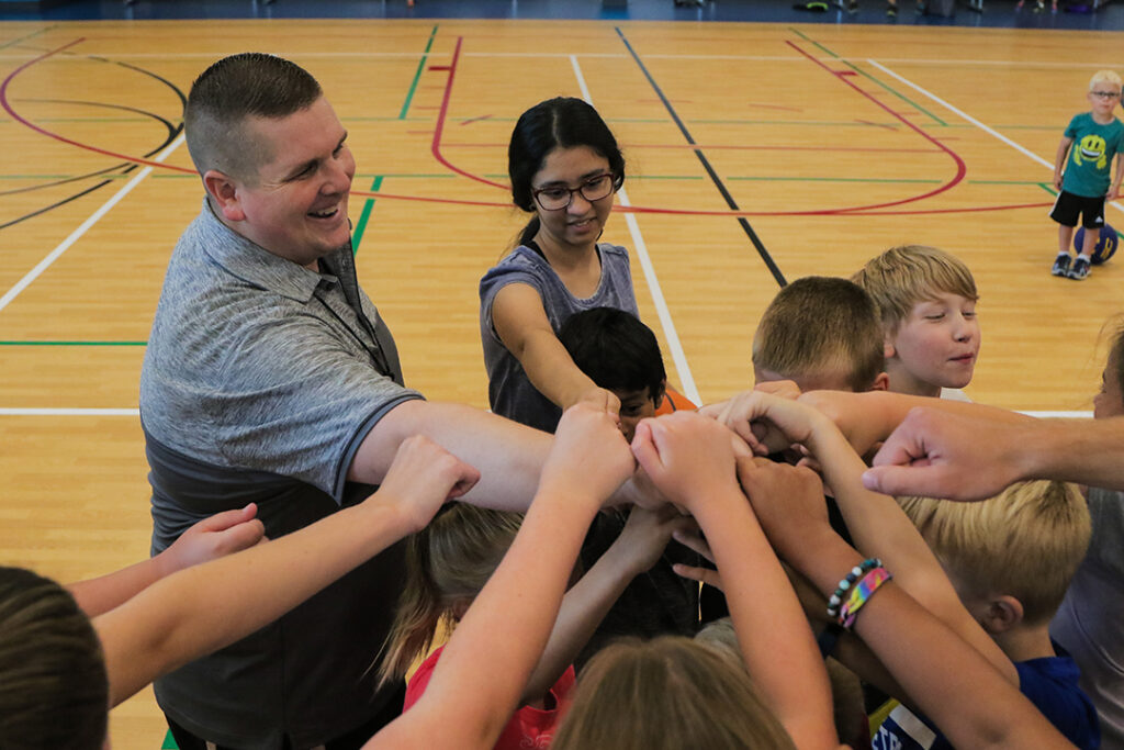 Basketball camp coach and campers huddle up on the court.