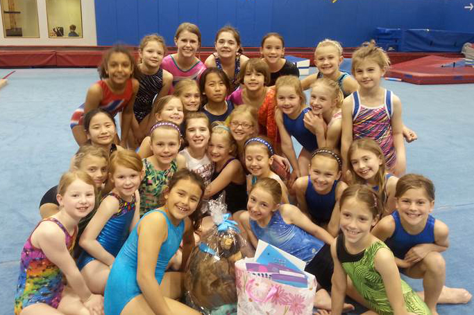 A gymnastics team of young girls gather and smile for the camera.