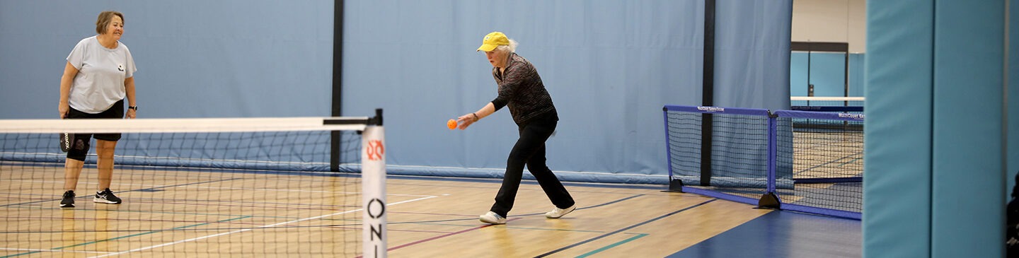 A senior gets ready to serve a pickleball.