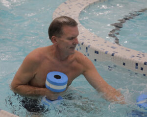 A man pushes foam barbells in a pool.