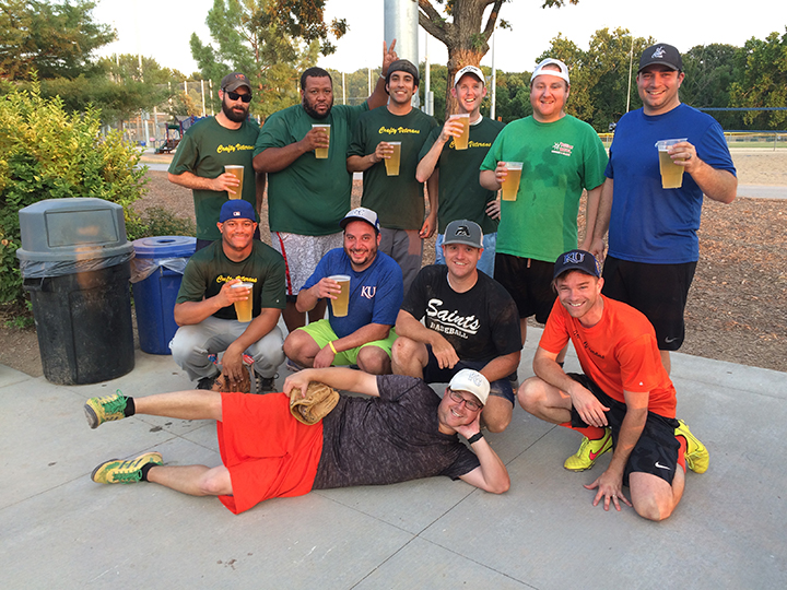 A group of men toasting each other with a beer after a softball game.