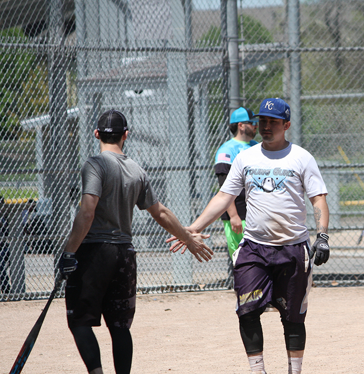 An adult softball player congratulates a teammate who just scored a run during an adult softball league game.