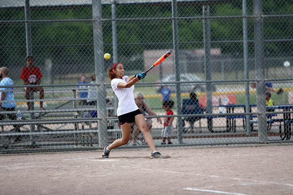 A female connects on a hit during an adult softball league game.