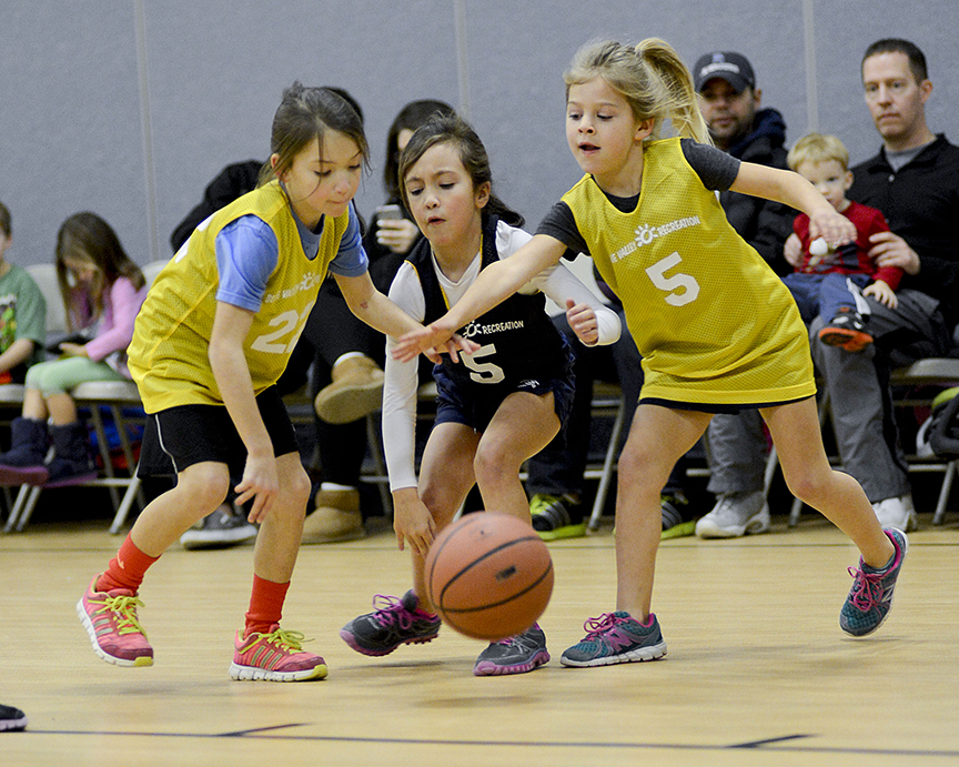 Three young girls reach for a basketball during a game.