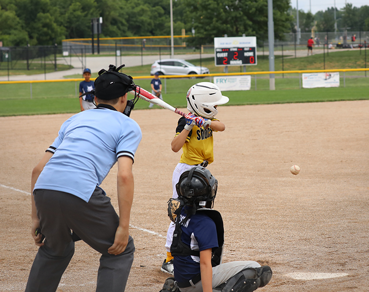 young boy batting in a baseball game with a catcher and umpire behind him.
