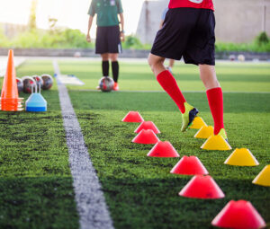 A teenager going through foot drills with red and yellow cones.