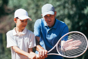 A coach instructs a young boy holding a tennis racquet.