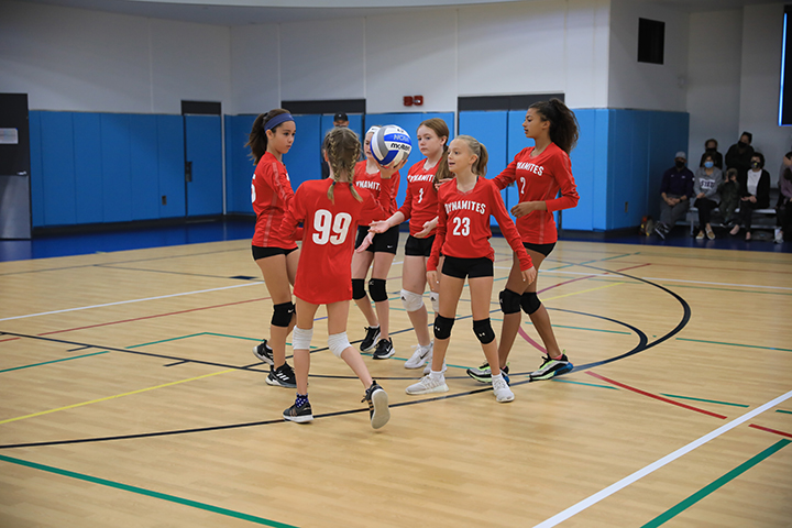 A youth softball team comes together on the court for a cheer during a youth volleyball tournament match.