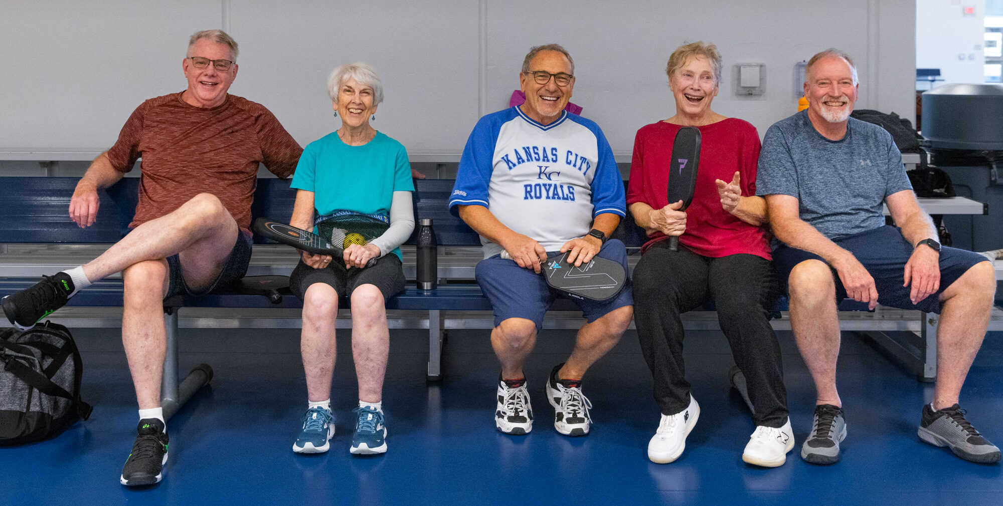 Pickleball players sit on a bleacher and smile after a game.