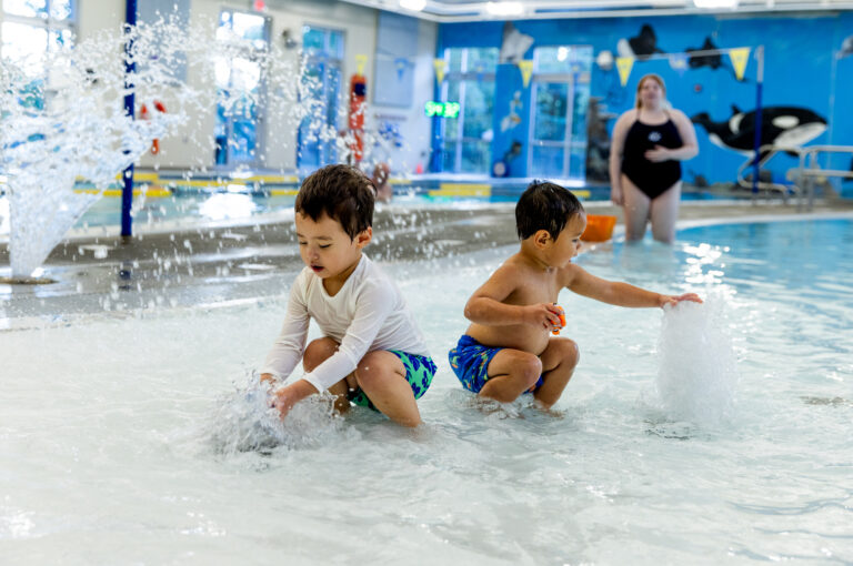 Two young boys play in the fountain feature of an indoor pool.