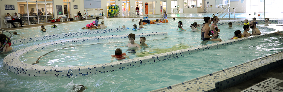 Kids and adults swim in an indoor pool.