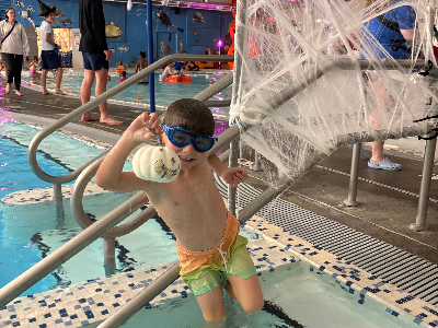 A young swimmer leans on the pool ladder and shows off the pumpkin he just retrieved from the pool.