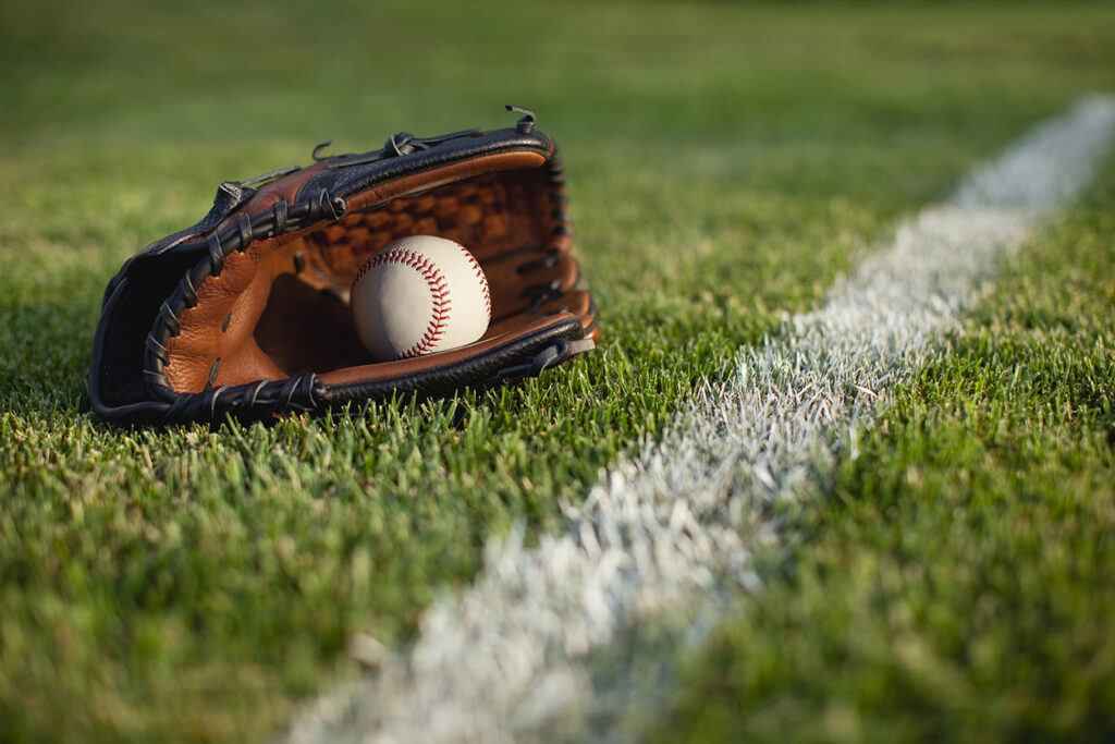 A baeball mitt lays in the grass by the white stripe.