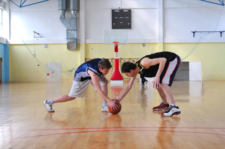 Two basketball players reaching for a loose ball.