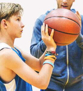 A player holds a basketball at eye level in the shooting position while a coach looks on.