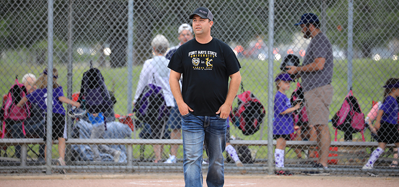 Executive Director Shane DeWald stands on a softball field coaching his youth team.