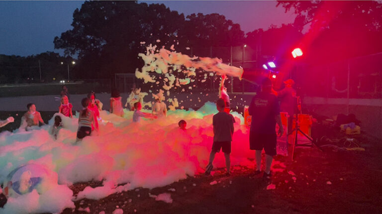 kids play in foam lit by colorful lights.