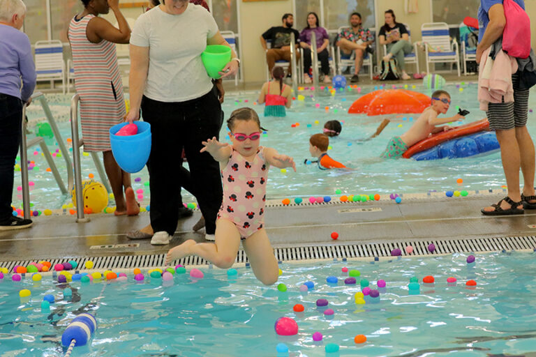 A young swimmer jumps into an indoor pool that has plastic eggs floating on top.
