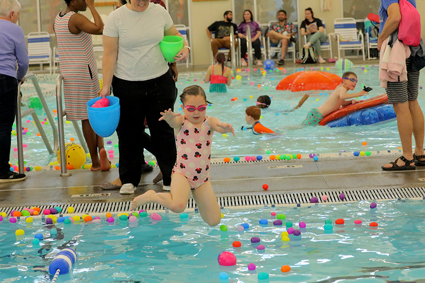 A young swimmer jumps into an indoor pool that has plastic eggs floating on top.