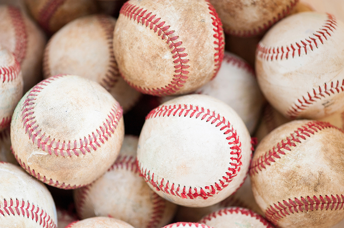 Pile of used baseballs with red stitching stacked together.