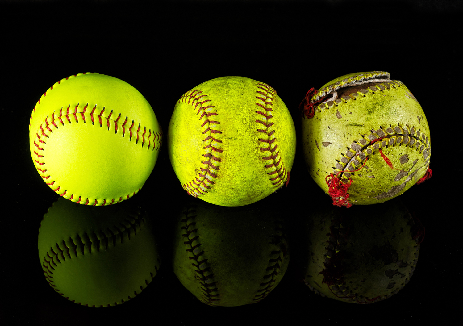 Three softballs showing new, used, and heavily worn conditions.