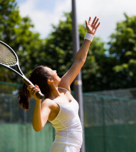 Adult tennis player serving the ball during a match on an outdoor tennis court.