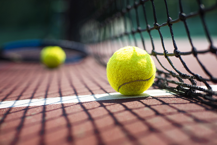Tennis ball resting beside the net on an outdoor tennis court.