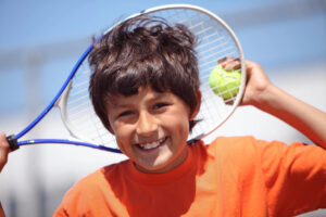 Young tennis player smiling while holding a racquet and tennis ball.