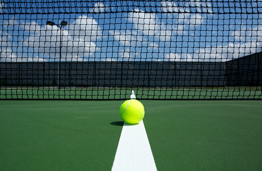 Tennis ball resting on the center line of an outdoor tennis court in front of the net.