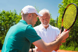 Tennis instructor demonstrating proper racquet grip to an adult player.