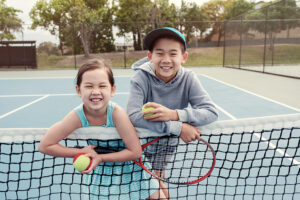 Two children smiling and holding tennis balls and racquets.