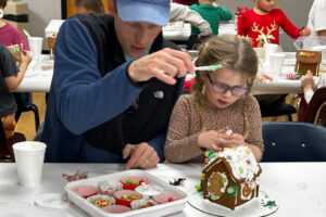 A family decorates a gingerbread house.